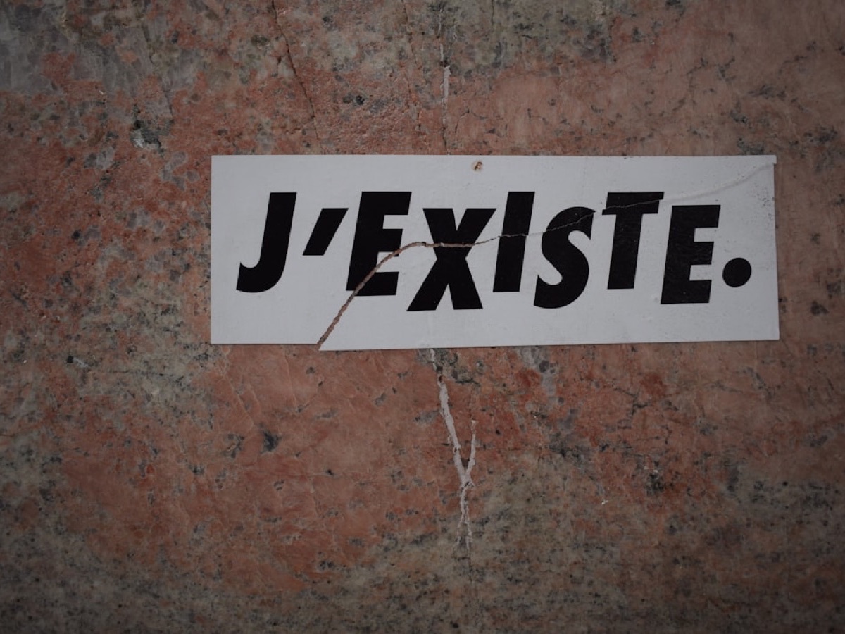 Autocollant « J'existe » collé sur un mur, métaphore du contenu SEO invisible