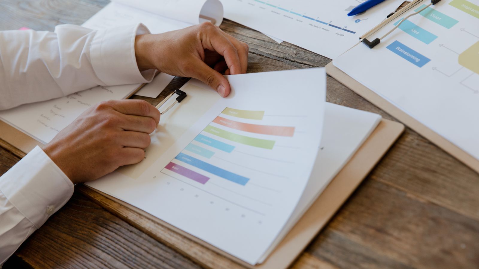 Mains feuilletant un rapport imprimé présentant des graphiques en barres colorés.