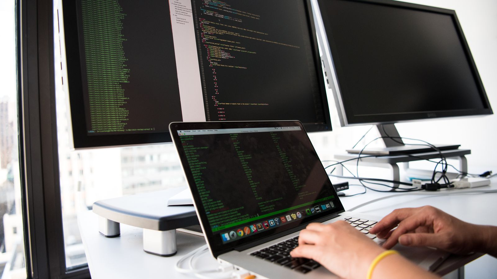 Développeur au travail sur un ordinateur portable devant plusieurs écrans affichant du code.
