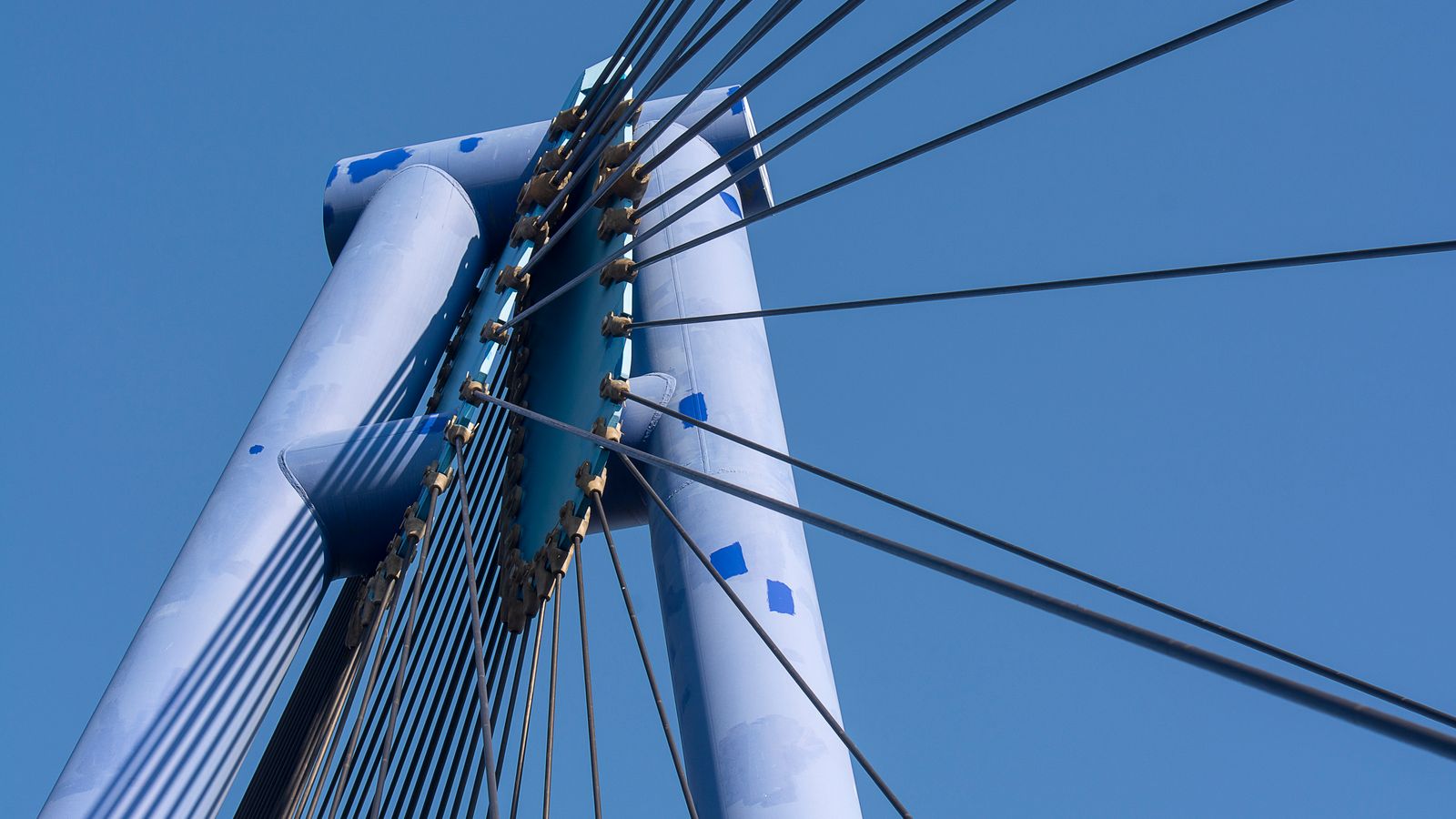 Câbles d'un pont haubané convergeant vers un pylône central sur ciel bleu, image d'un maillage de liens.